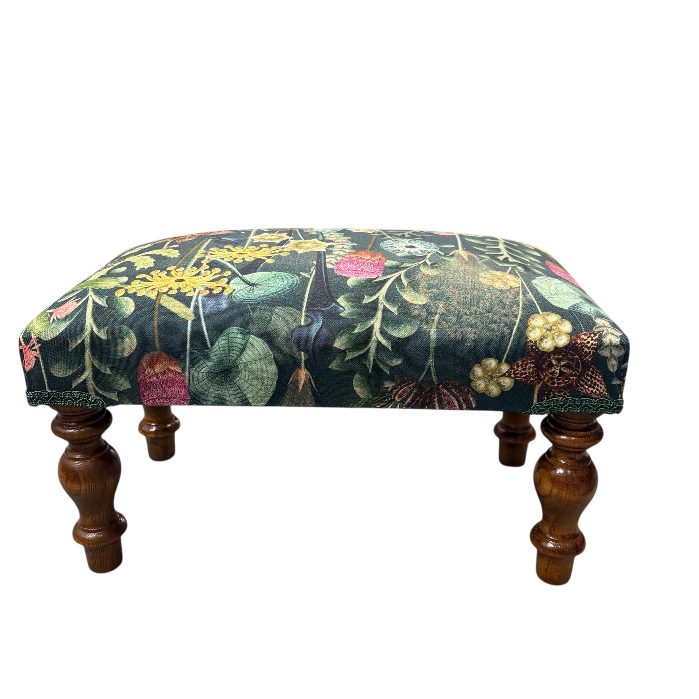 A beautiful hand crafted footstool covered in a dark green cotton featuring a botanical scene in dark green fabric with mahogany stained legs.
