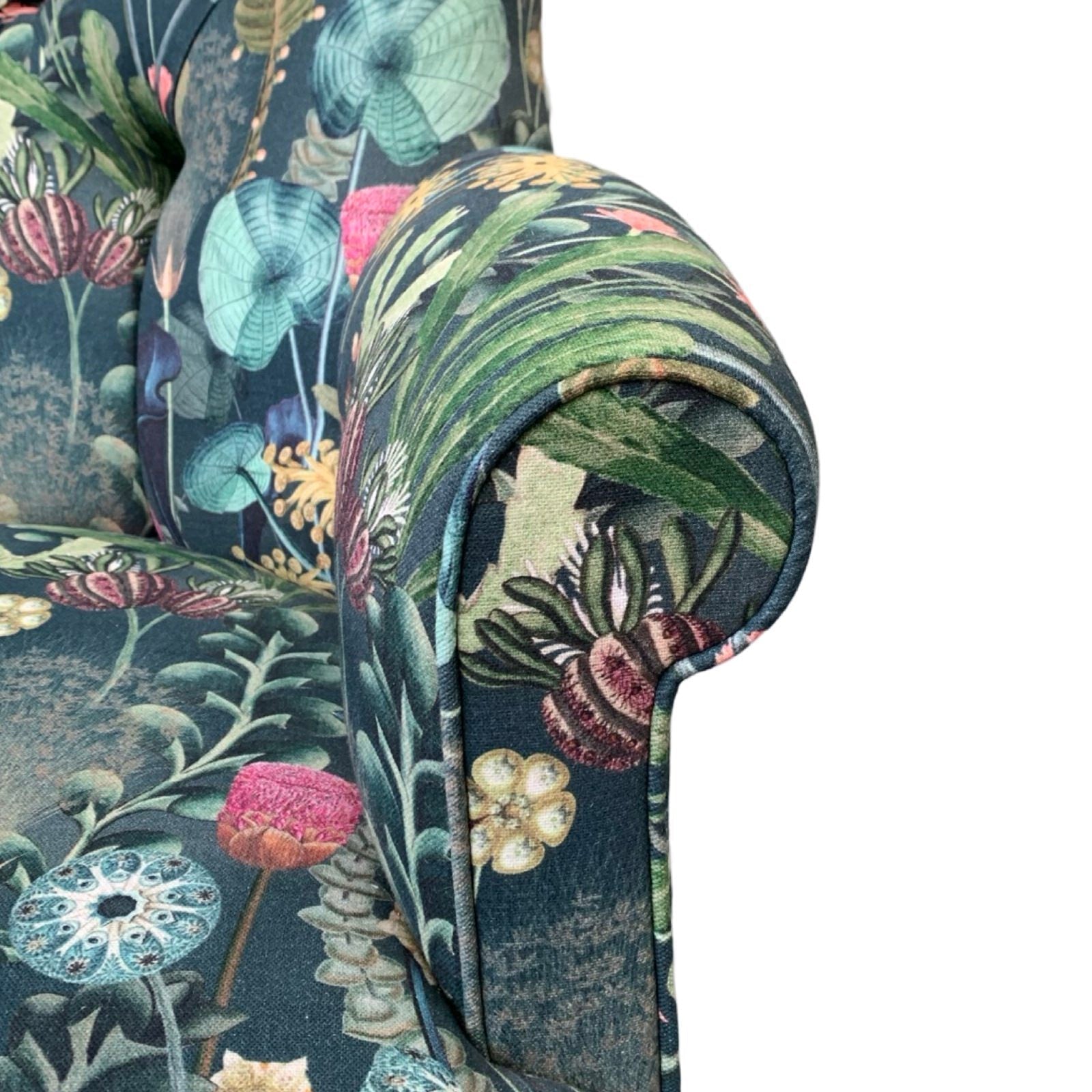 A dark green linen armchair with a turquoise, mustard, pink, and green botanical design, featuring a button-back and mahogany legs with gold castors.