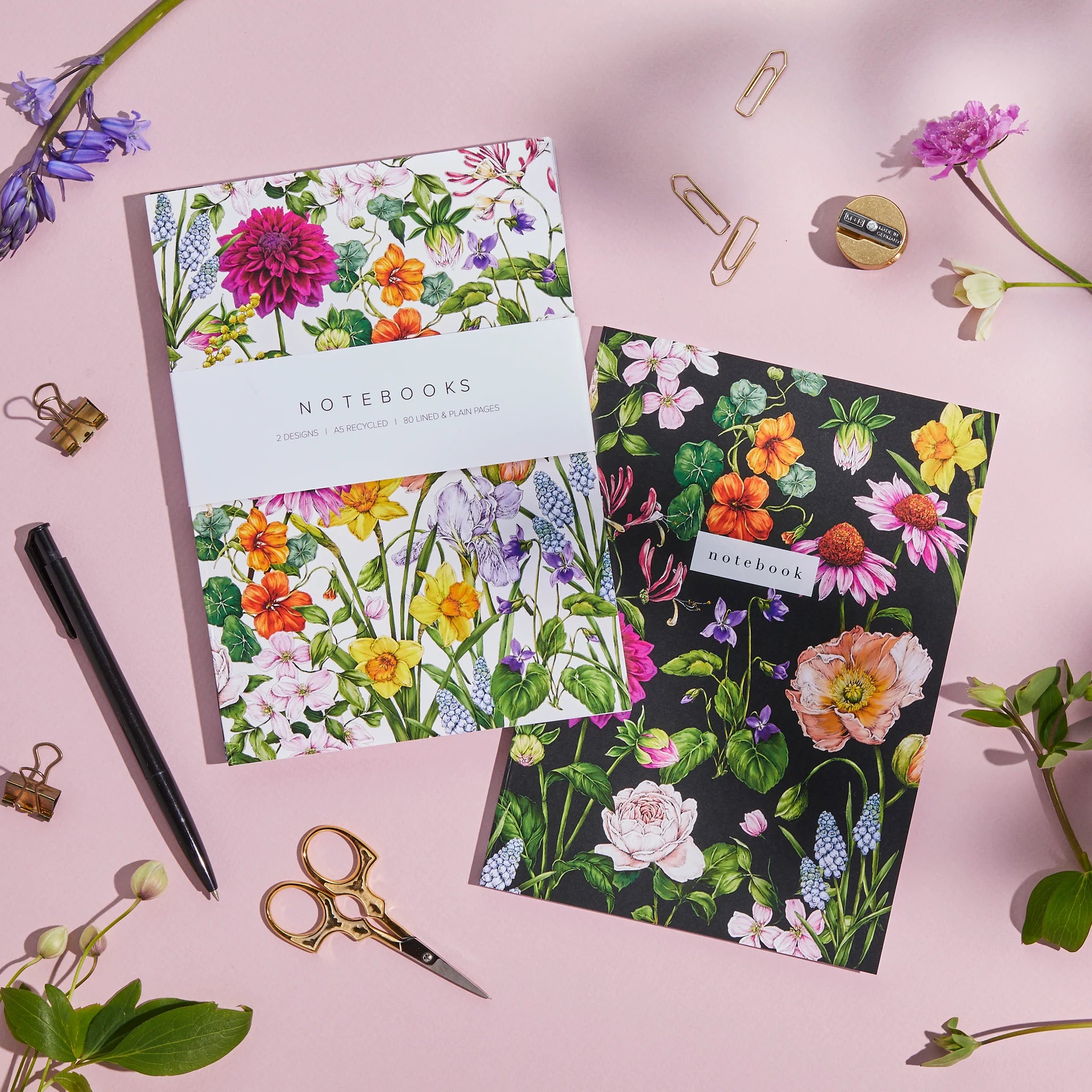 Two floral notebooks on a pink background with stationery items.