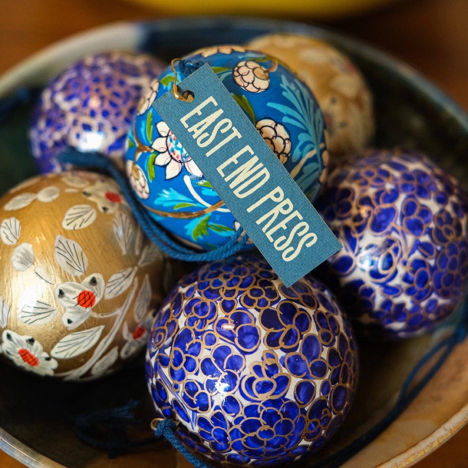 A bowl of round papier mache Christmas baubles in gold, navy and cobalt blue.