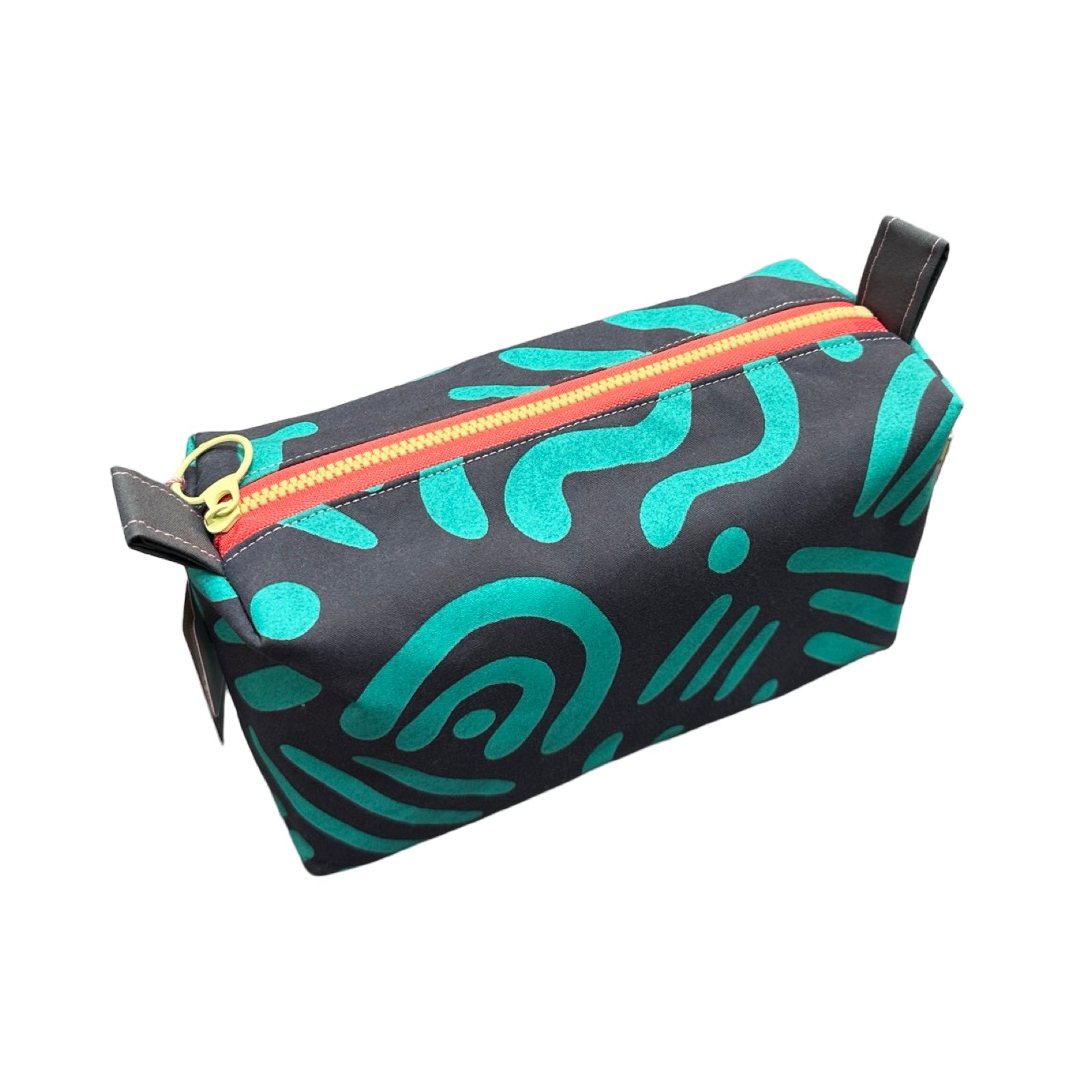 A grey boxy cosmetic bag with a turquoise abstract design.