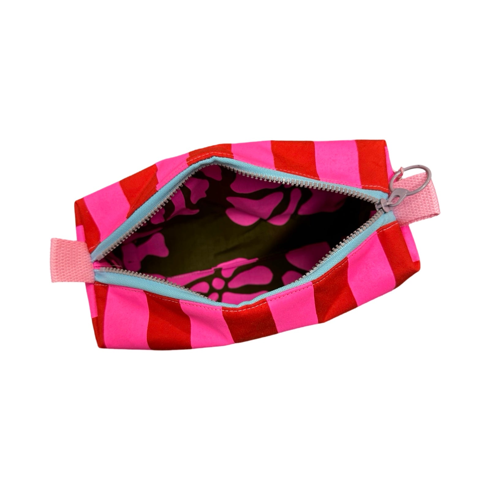 A boxy cosmetic bag in red and bright pink stripes open showing grey and pink floral lining fabric.