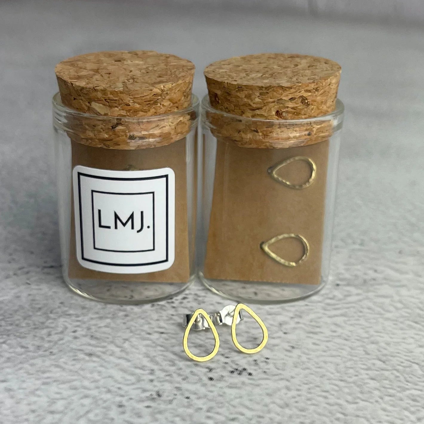 Two glass jars with cork lids and gold earrings on a textured surface.