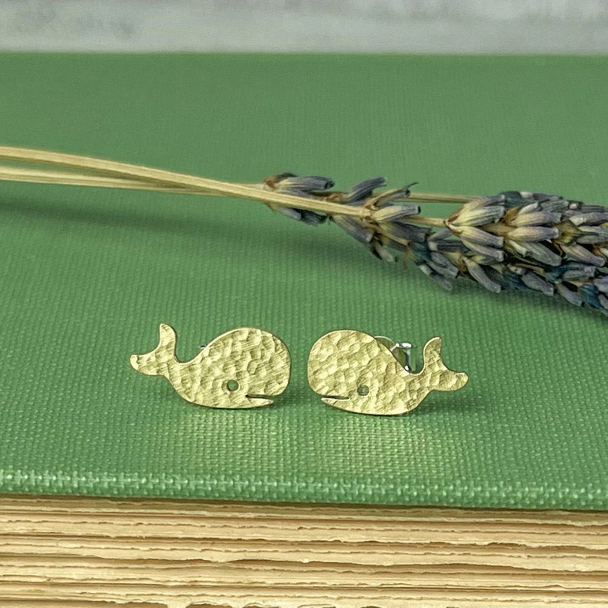 Gold whale-shaped earrings on a green surface with lavender.