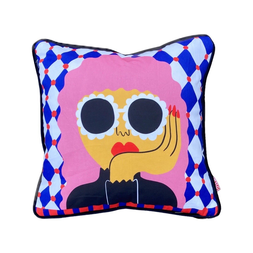 Colourful cushion featuring a lady with pink hair, holding her head in one hand, wearing huge white floral sunglasses, against a blue and white checked background.