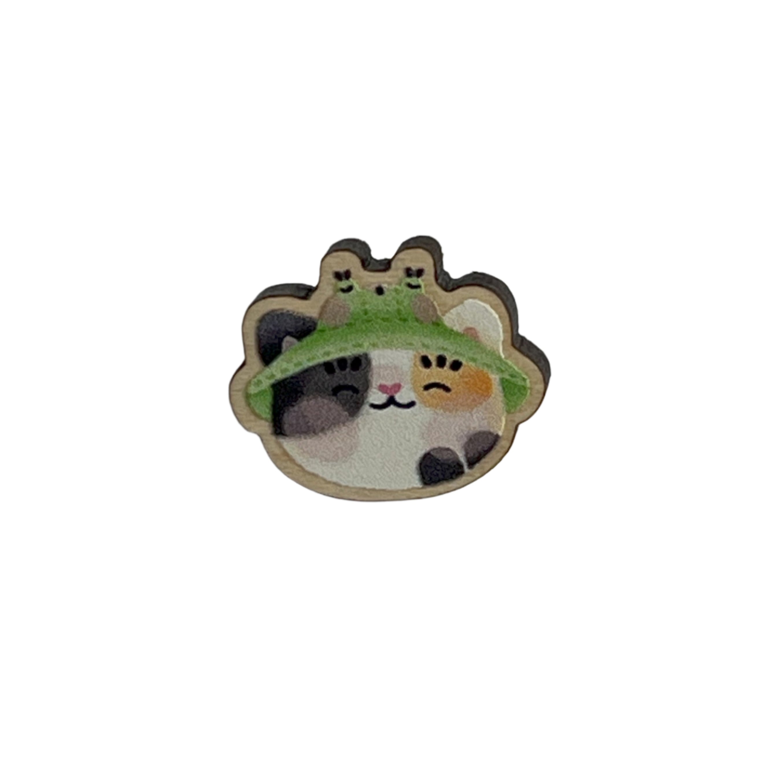 Mini wooden pin badge of a calico cat wearing a frog bucket hat. This badge is printed onto 3mm thick responsibly sourced European birch plywood.