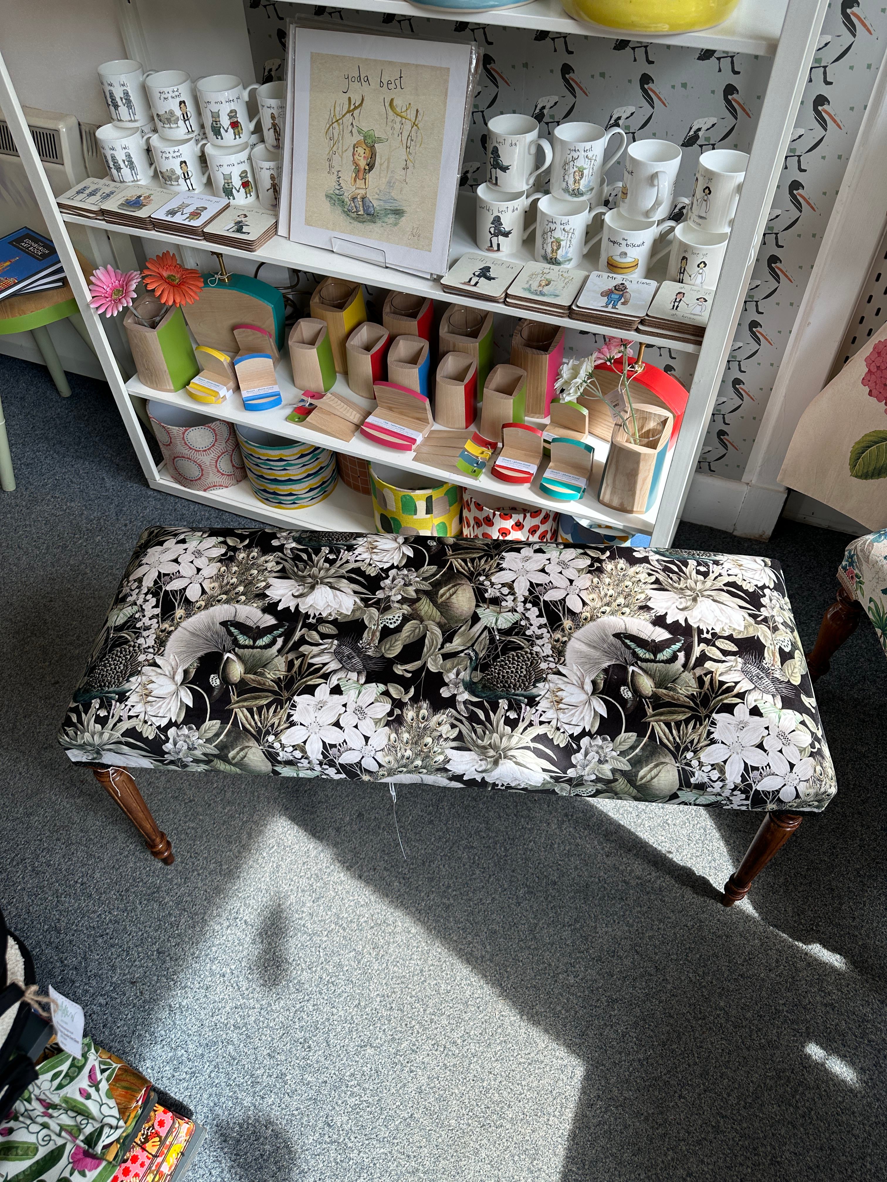 Floral-patterned bench next to a shelf with decorative items on a carpeted floor.