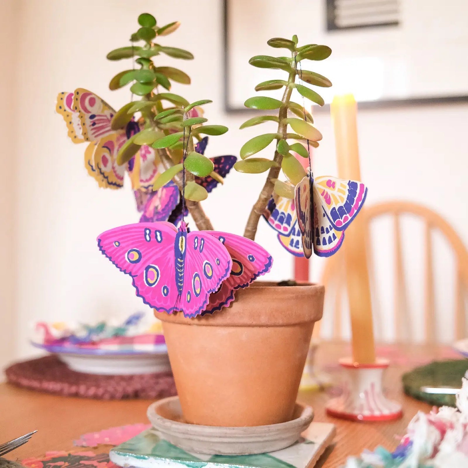 4 pink, yellow and purple paper butterfly decorations hanging from a potted plant.