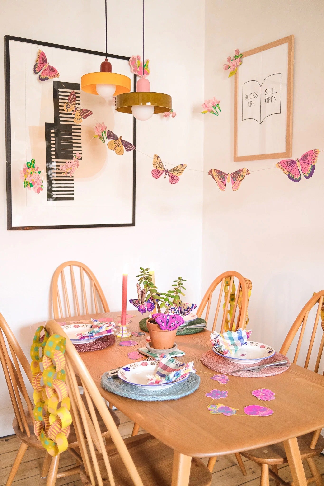Dining room with wooden table and chairs, colourful butterfly decorations, and framed artwork on the wall.