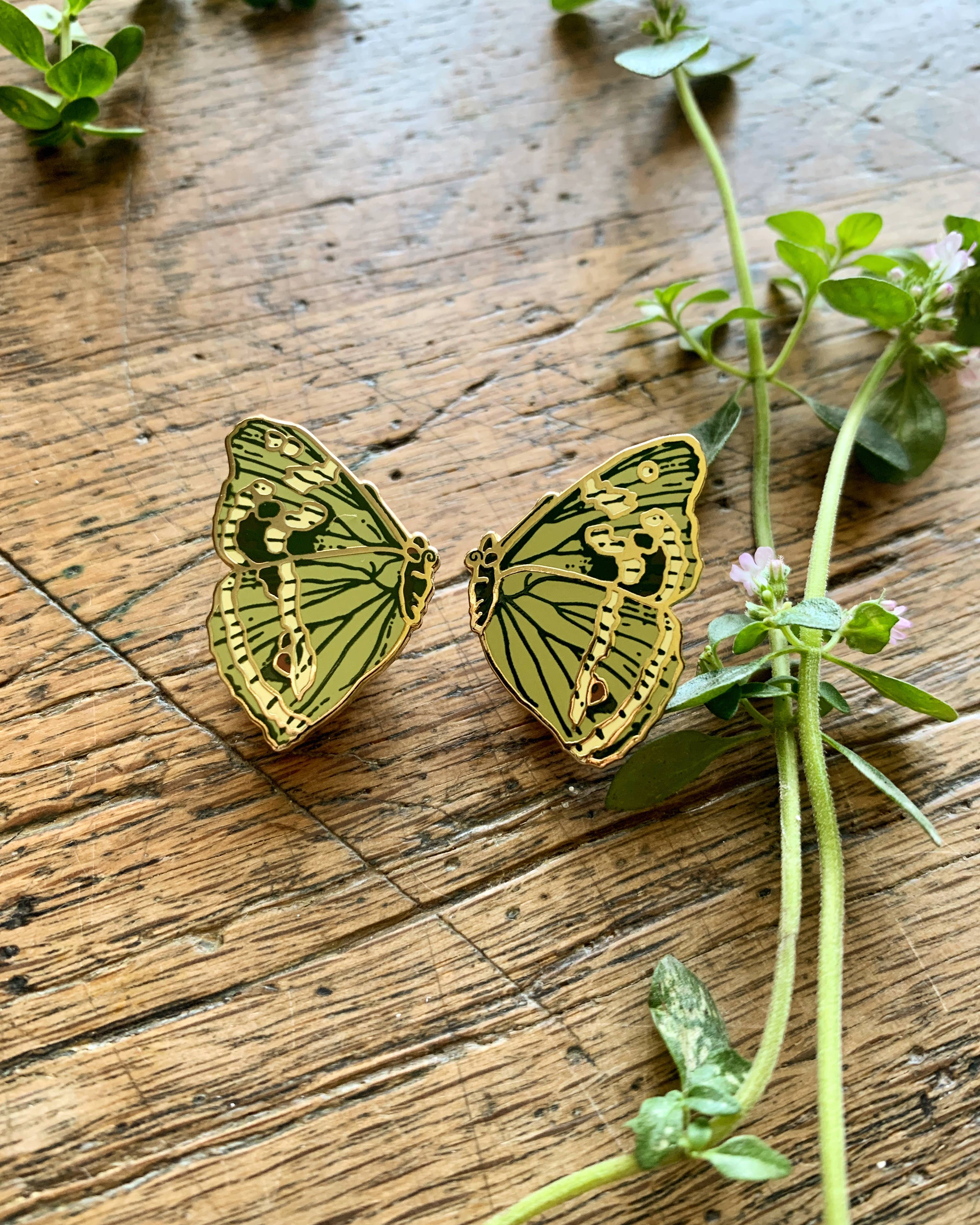 Butterfly-shaped pin badges on a wooden surface with green leaves.