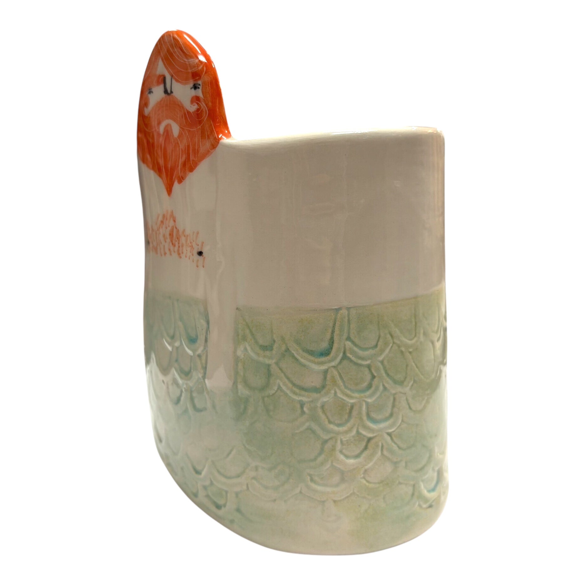 The side of a handmade ceramic pot with pale green mermaid scales and a man's head with ginger hair and a beard.