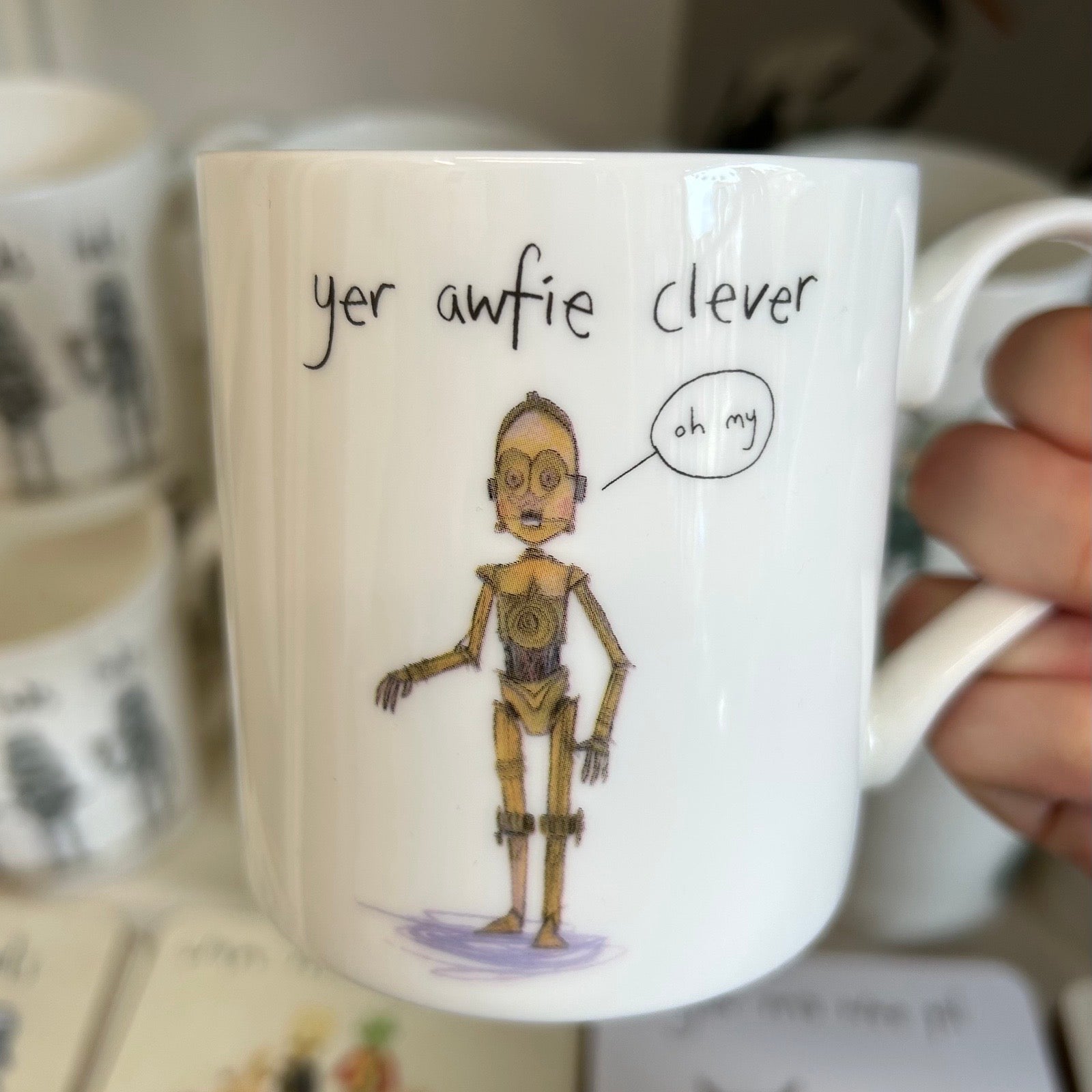 Mug with a cartoon C3PO and text 'yer awfie clever oh my' held by a hand.