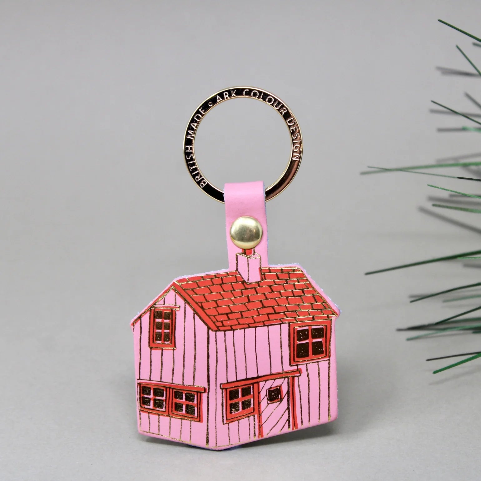 Pink house-shaped keyring with a gold accent on a grey background.