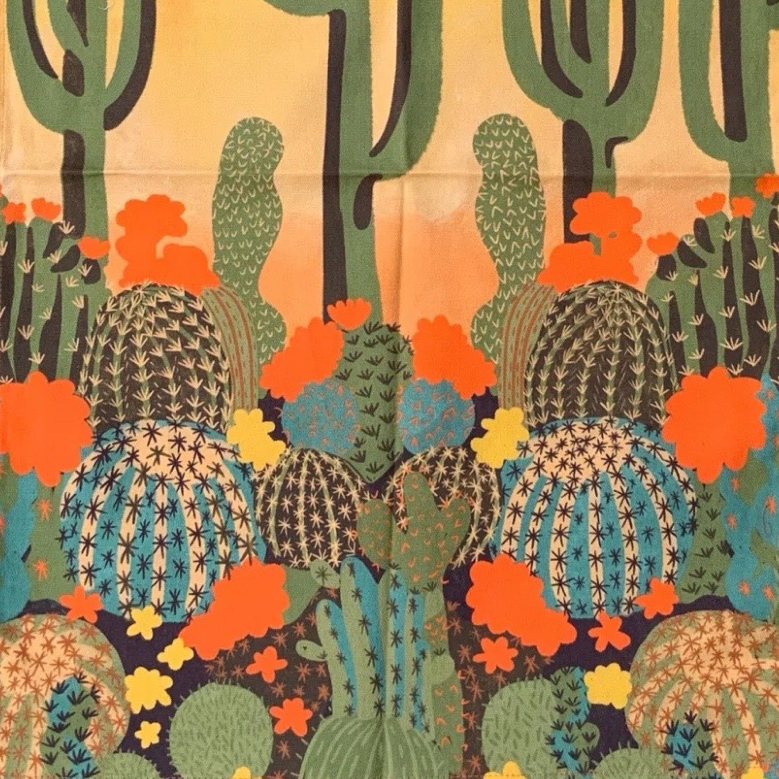 Close up of a tea towel with a cactus design on an orange background.