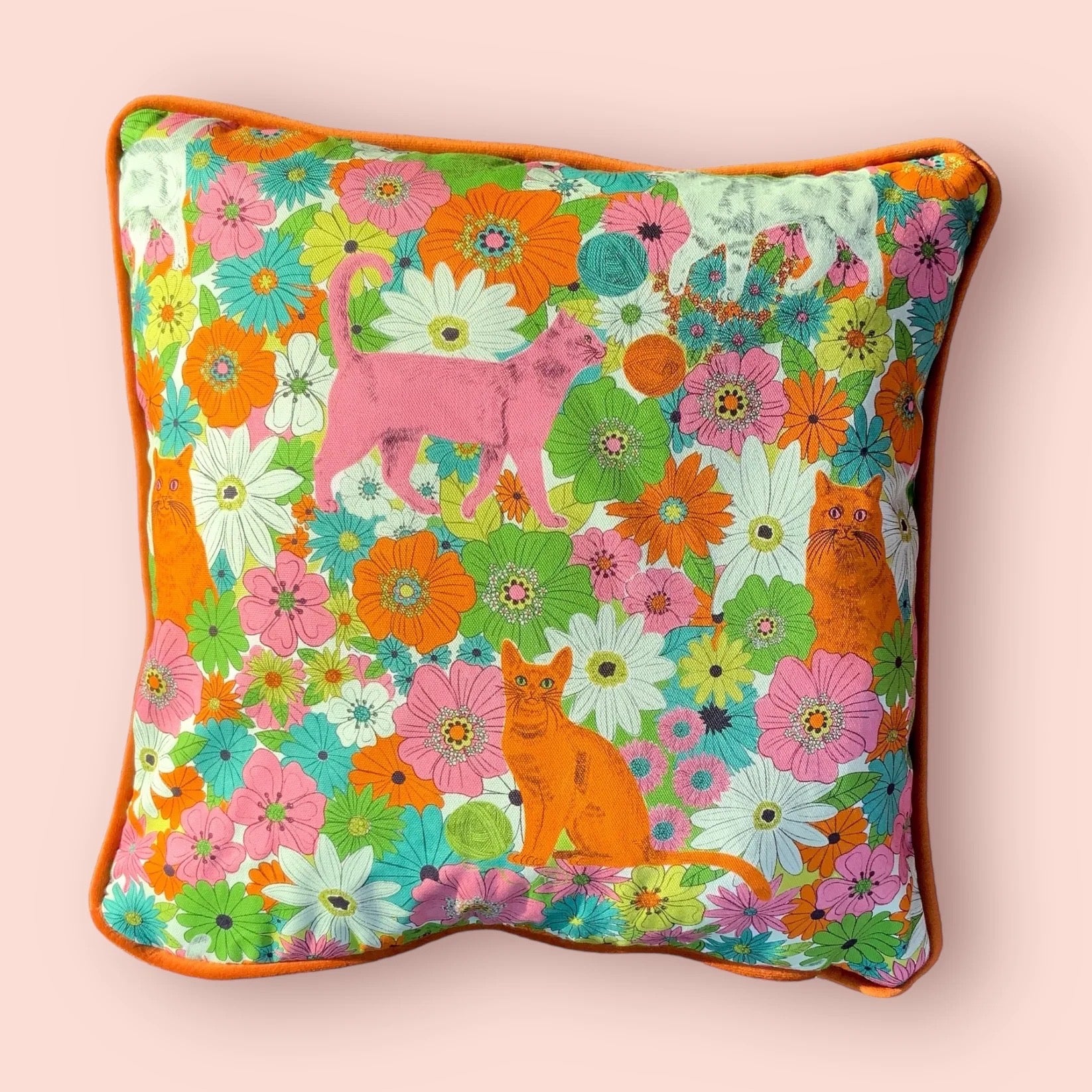 Colourful pillow with floral patterns and cat illustrations on a pink background.
