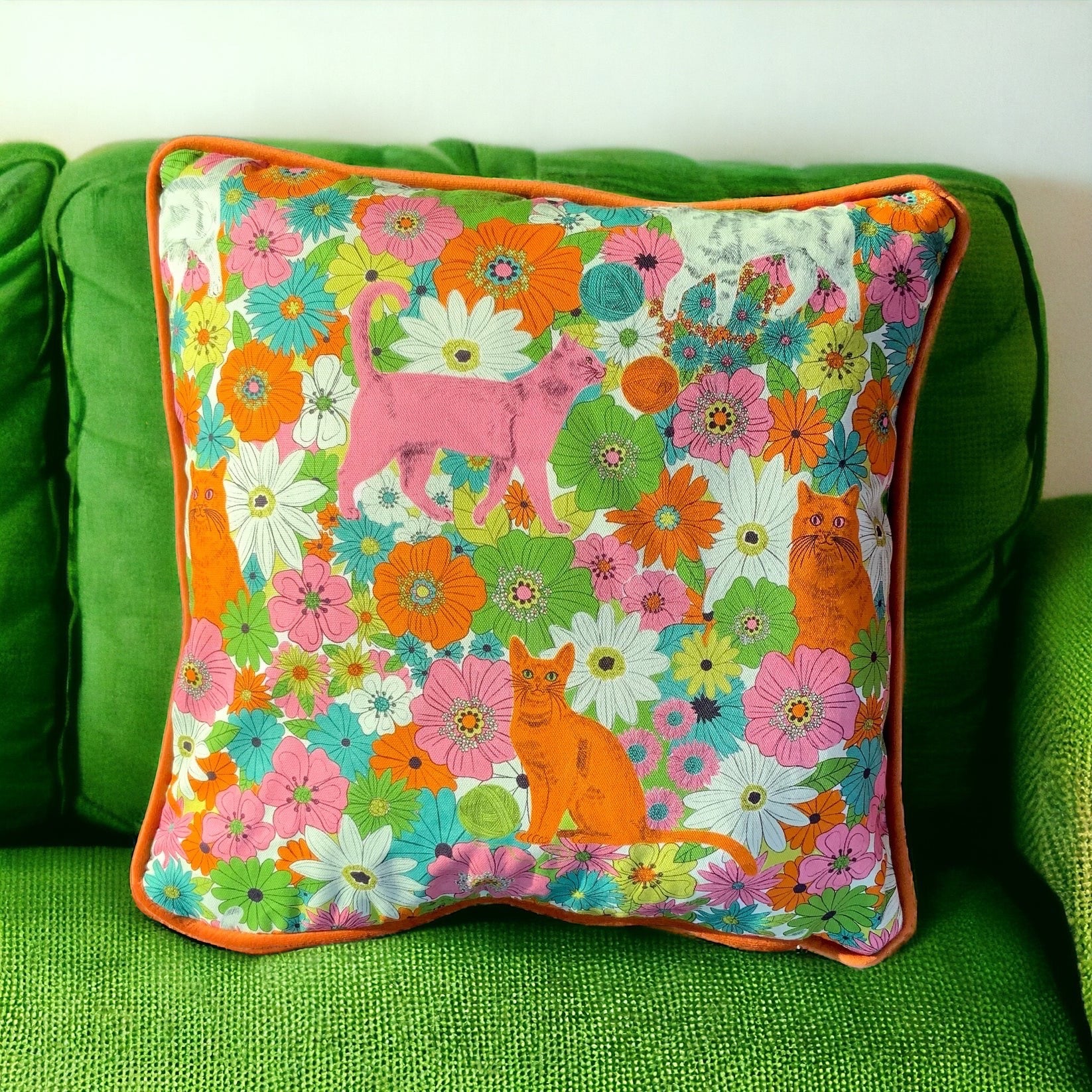 Colourful cushion with floral patterns and cat designs on a green couch.