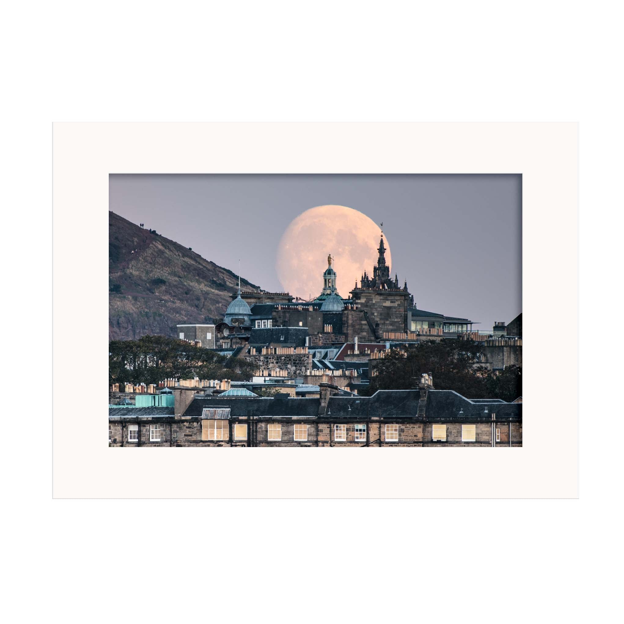 An image of a moon rising behind some buildings in a white mount.