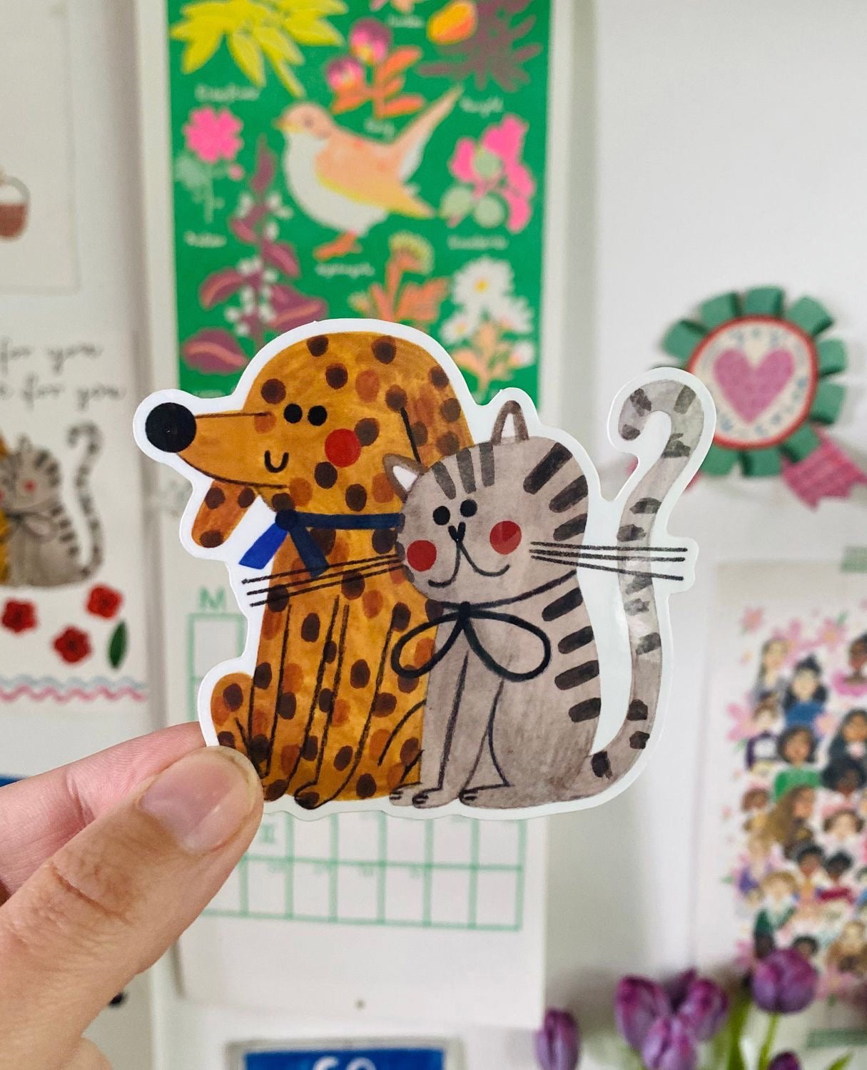 Hand holding a sticker of a dog and cat together with a colourful background.