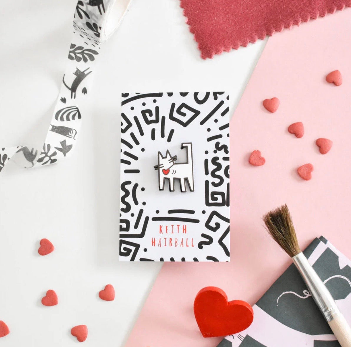 Cat pin badge on a white and black abstract card, on a table with craft supplies.