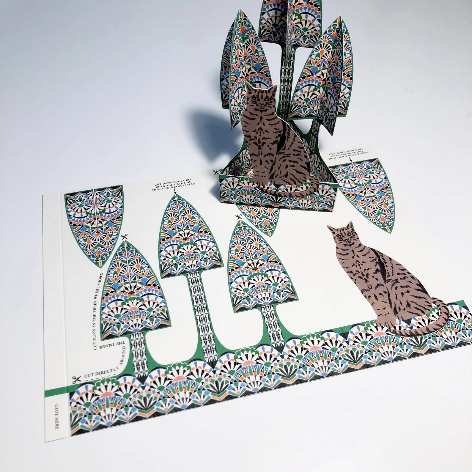 Decorative paper cutout of a cat and trees with intricate patterns on a white background.
