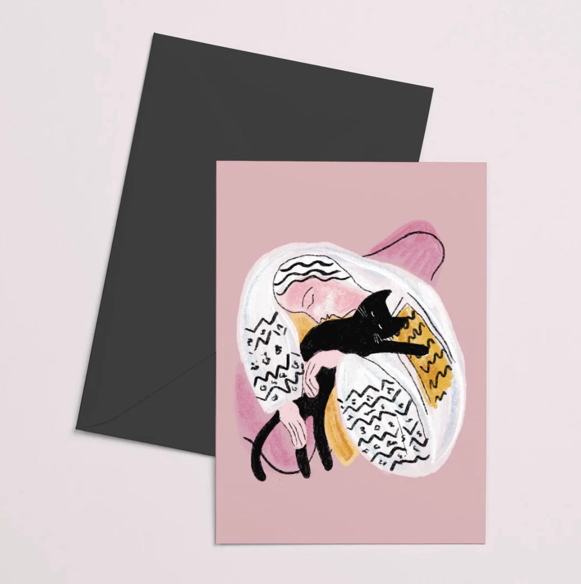Greeting card with an illustration of a person holding a cat, paired with a black envelope on a light pink background.