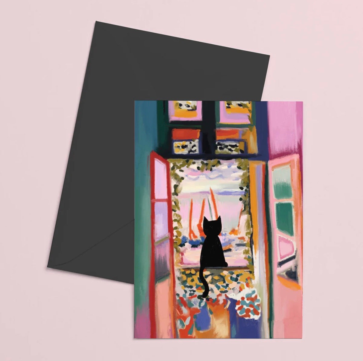 Greeting card with a black cat silhouette in front of a colorful window, paired with a black envelope on a light pink background.