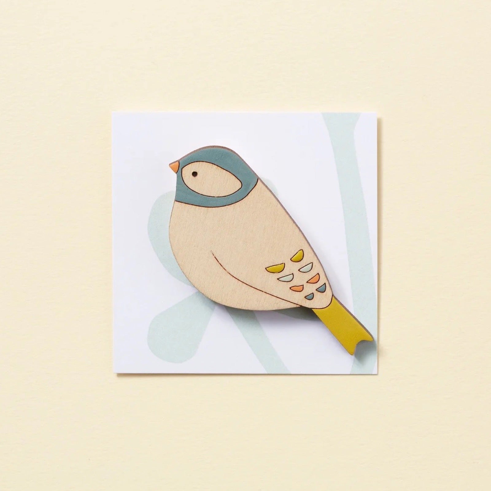 Wooden bird-shaped brooch on a white card with a light yellow background.