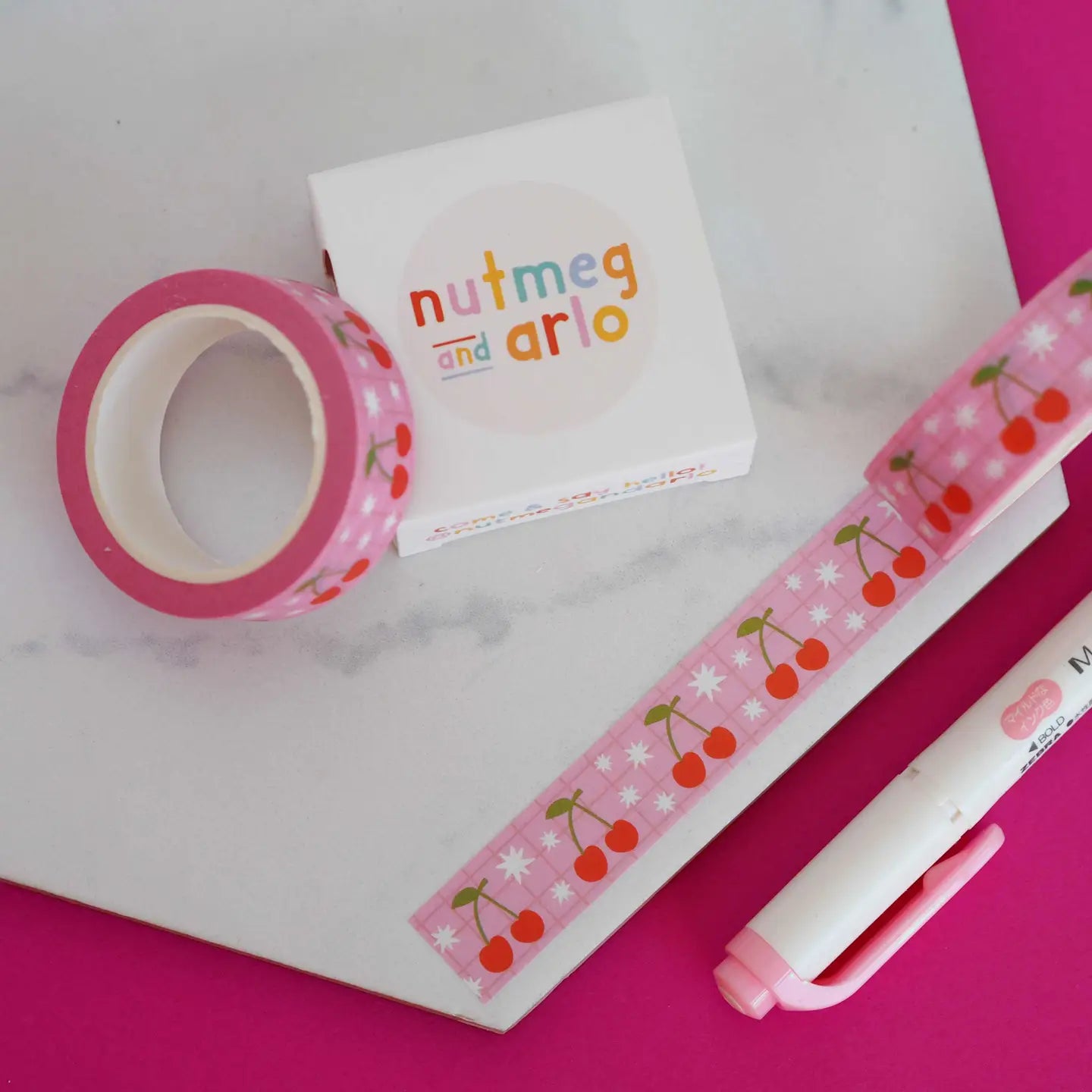 Decorative tape, washi tape, and pen on a pink and white background.