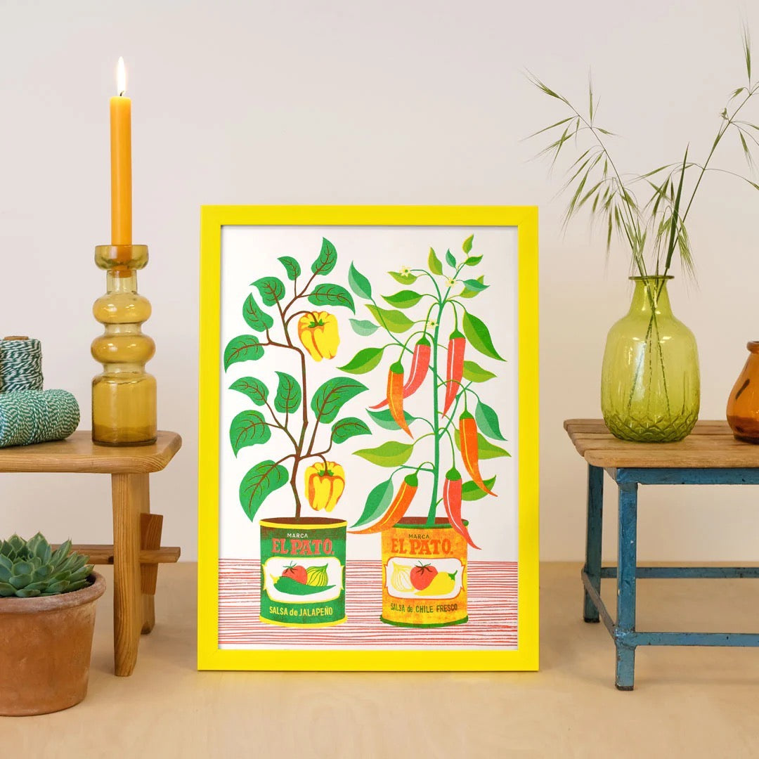 Framed artwork of plants growing out of cans on a wall with decorative plants and candles.