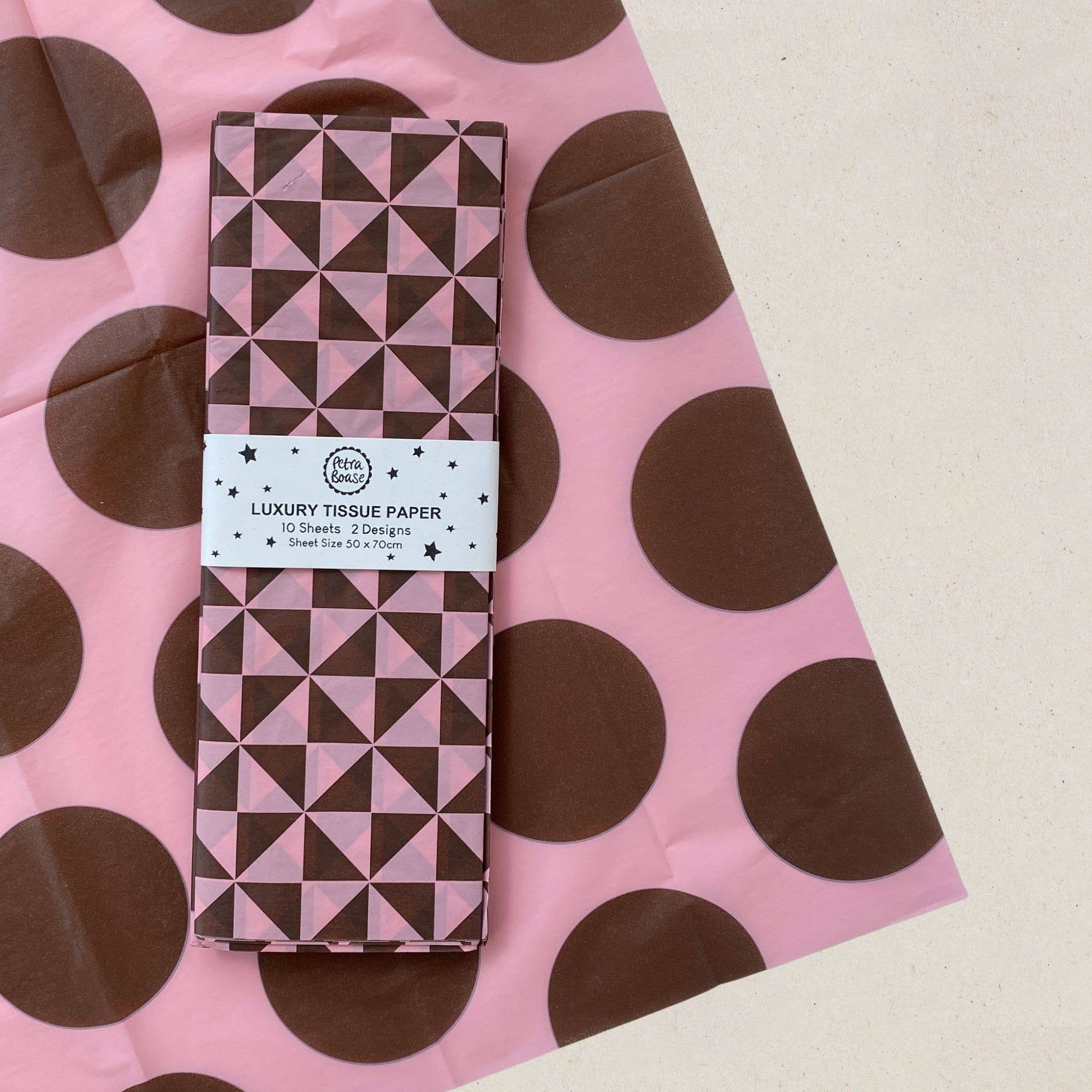 A roll of patterned luxury tissue paper wrapped in a white paper band labeled 'LUXURY TISSUE PAPER' placed on top of a pink tissue paper sheet with large brown polka dots.