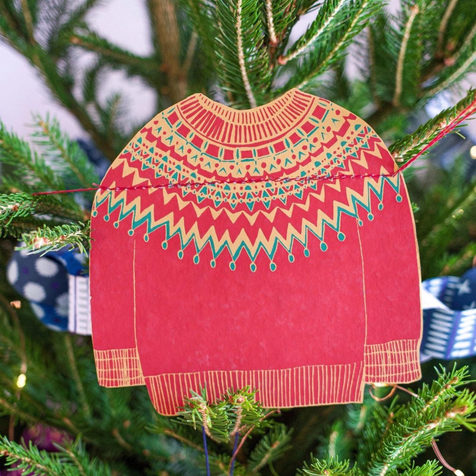 A red and green patterned paper jumper hanging on a Christmas tree.