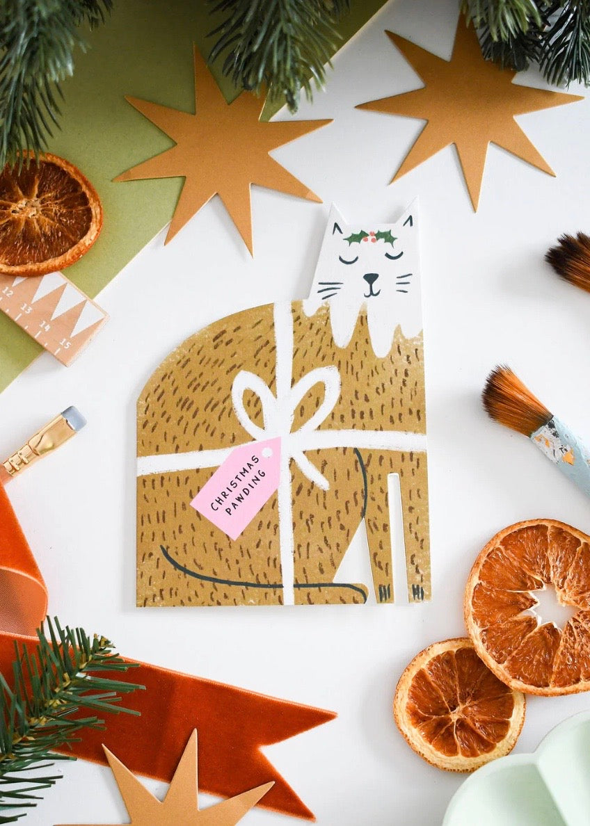 Card with cat design surrounded by Christmas decorations on a white background.