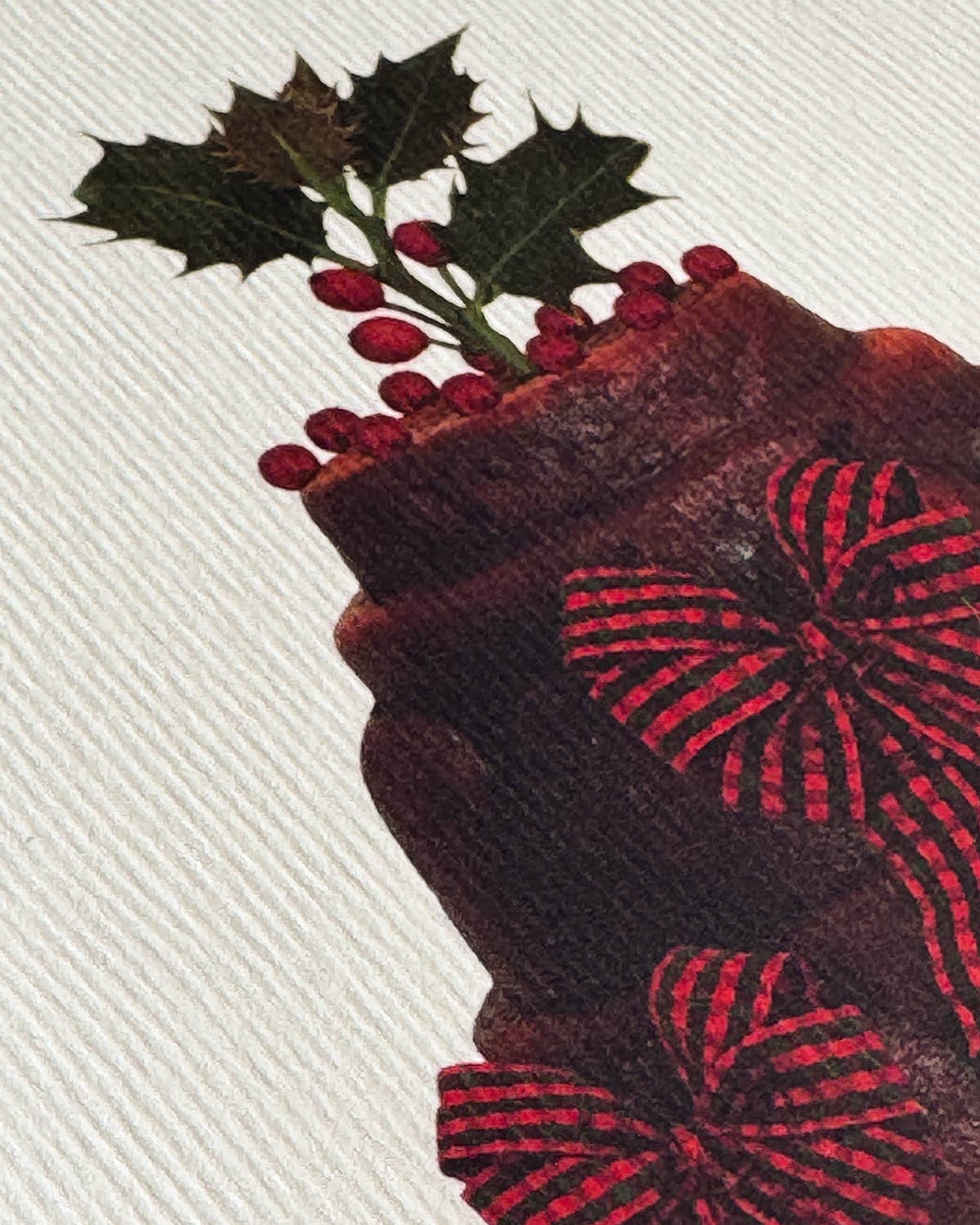 Close-up of a red fabric with floral patterns and holly leaves on a white background.