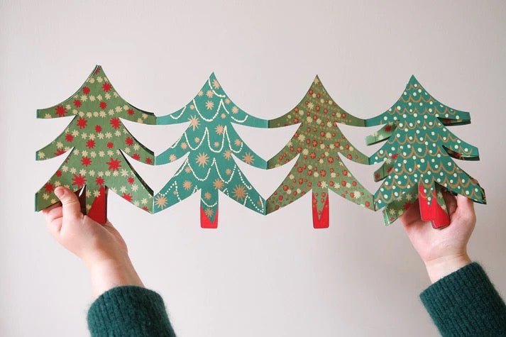Two hands holding four paper Christmas trees with patterns on a light background.