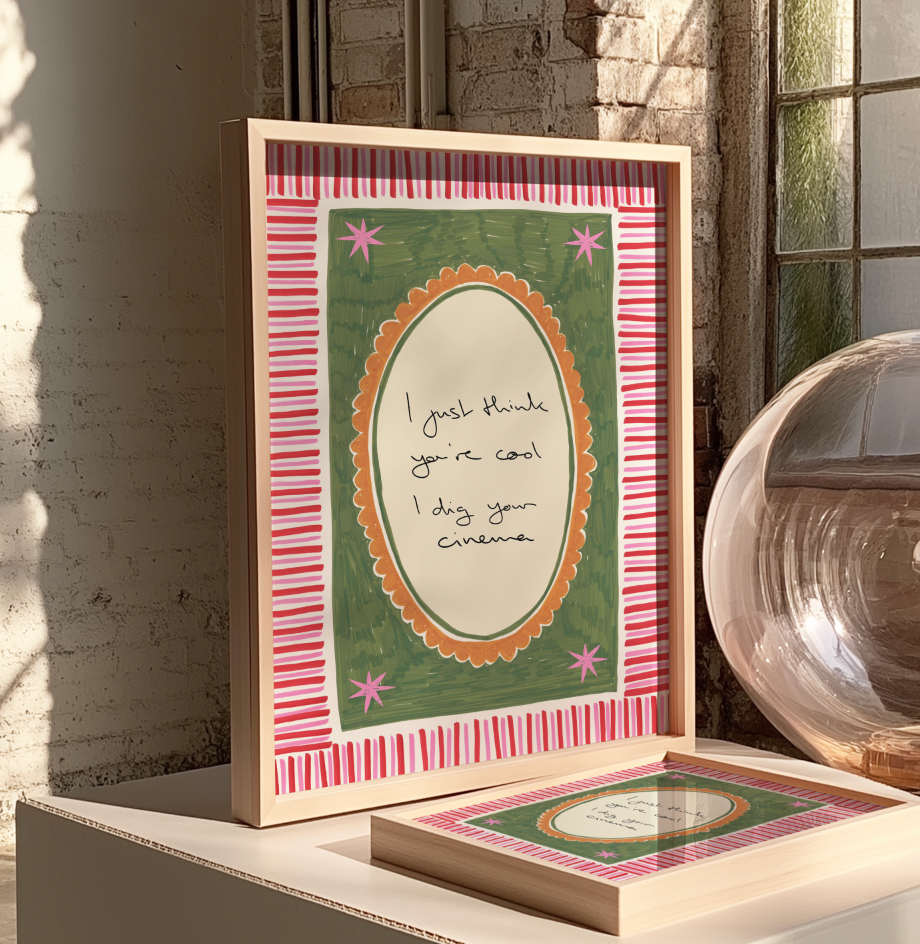 Framed print with decorative border and text on a surface with a window and brick wall background.