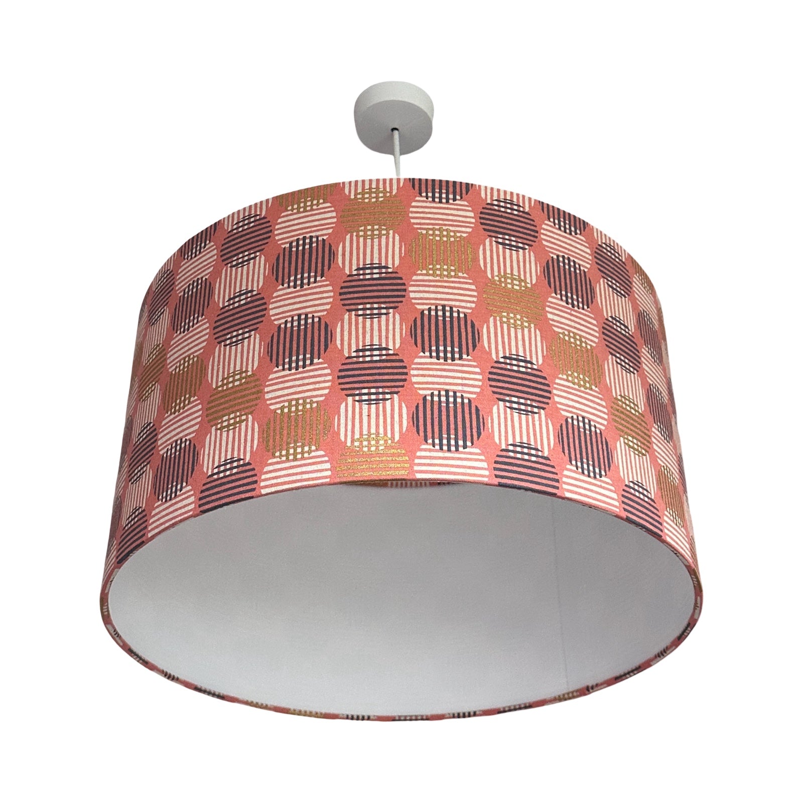 A drum lampshade covered in pink canvas fabric with navy, white, and gold striped circles.