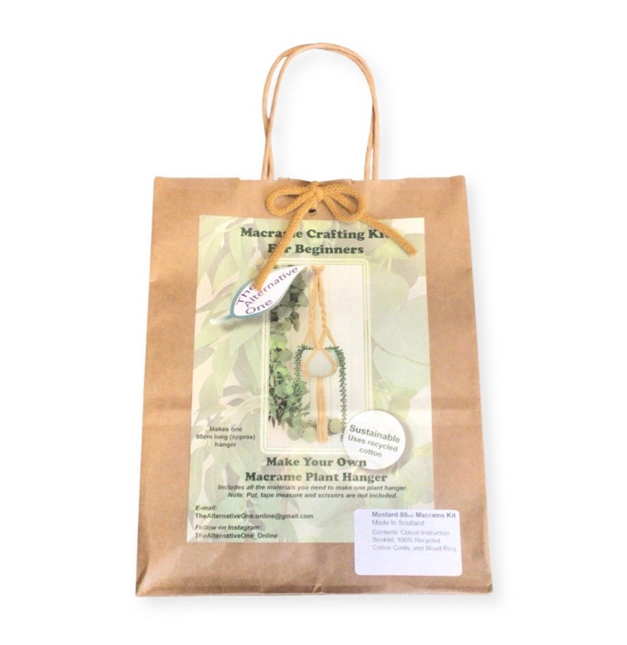 A Classic Macrame Plant Hanger Kit packaged in a brown paper bag displaying the contents, including pre-cut macrame cords and a wooden hanging ring.
