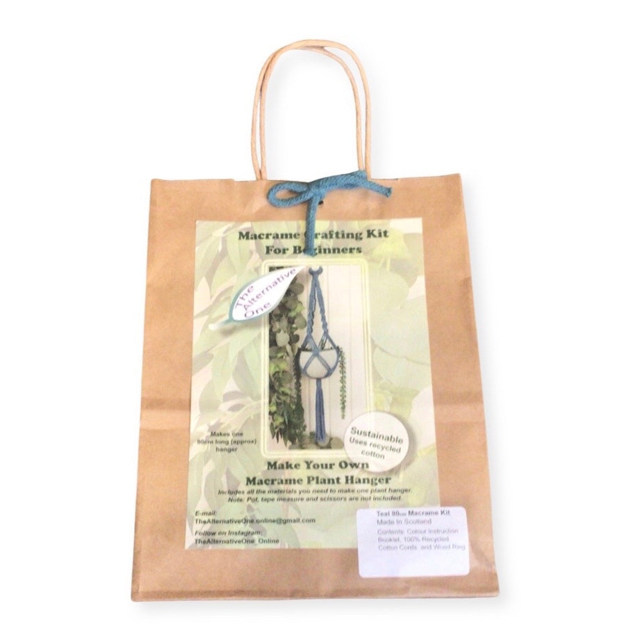 A Classic Macrame Plant Hanger Kit packaged in a brown paper bag displaying the contents, including pre-cut macrame cords and a wooden hanging ring.
