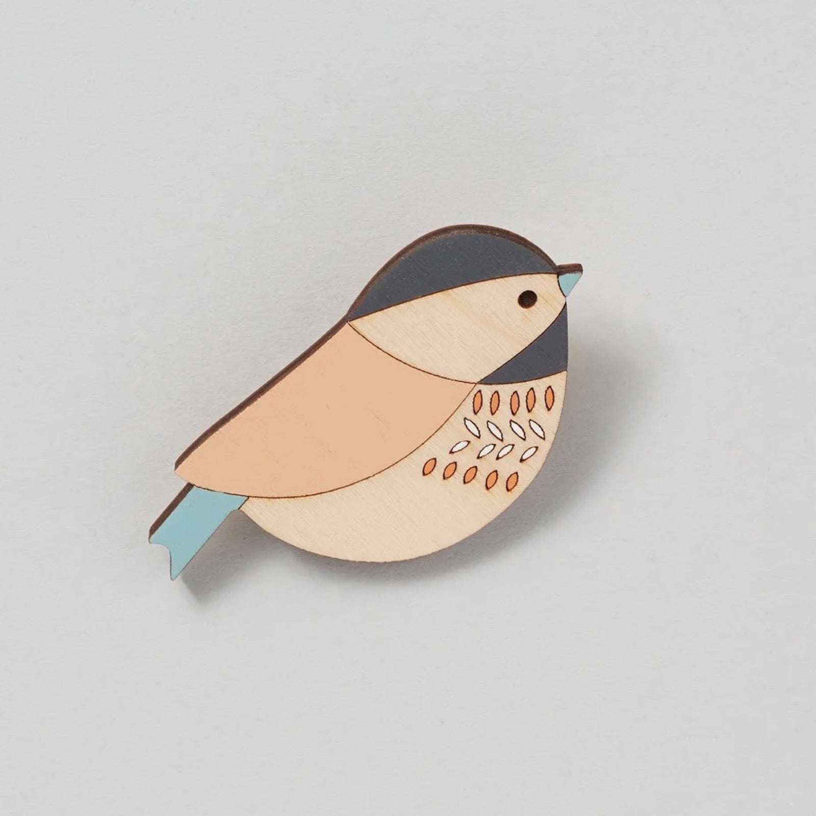 Wooden bird brooch on a light grey background.