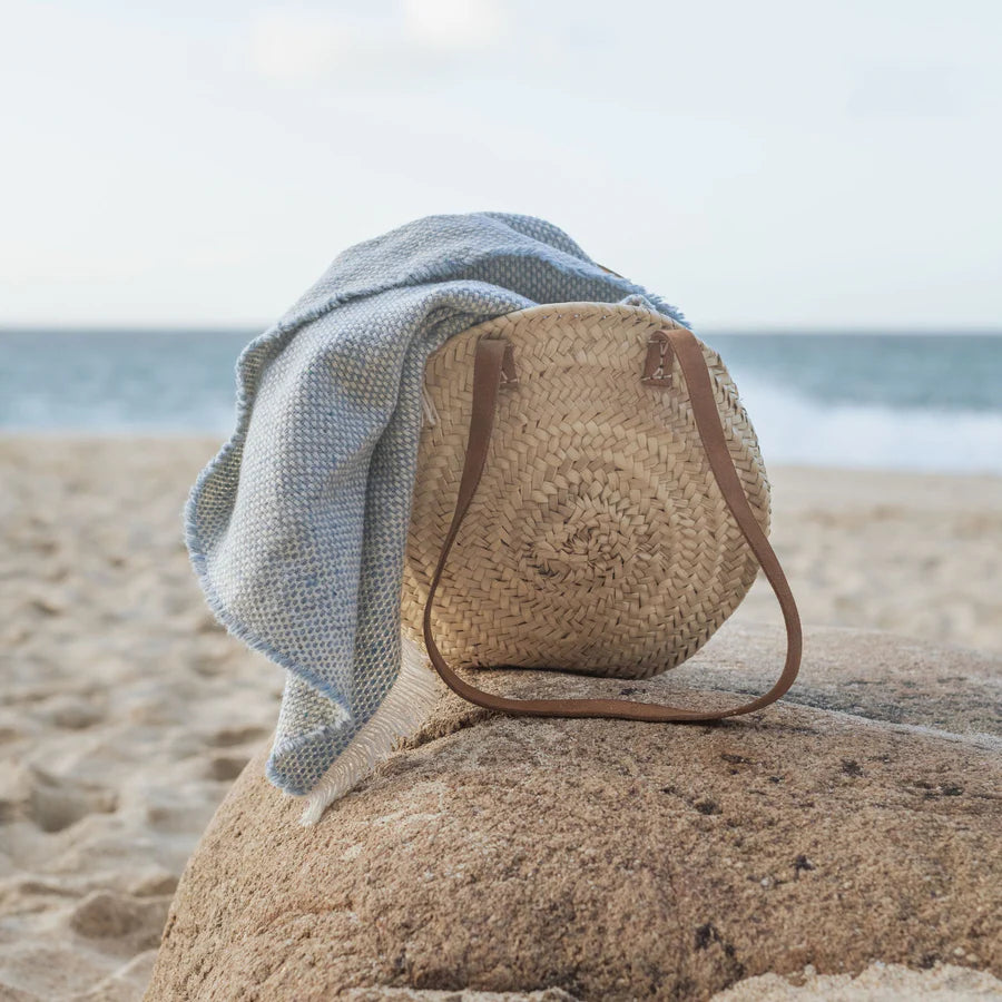 Woven bag with a blue blanket on a rock at the beach.