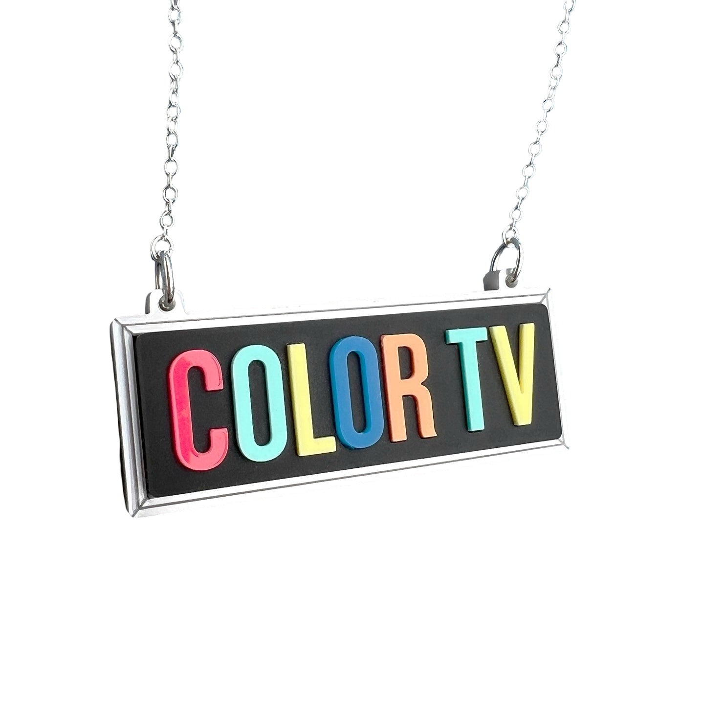 A necklace featuring a black rectangular acrylic pendant with the words COLOR TV in multicoloured lettering.