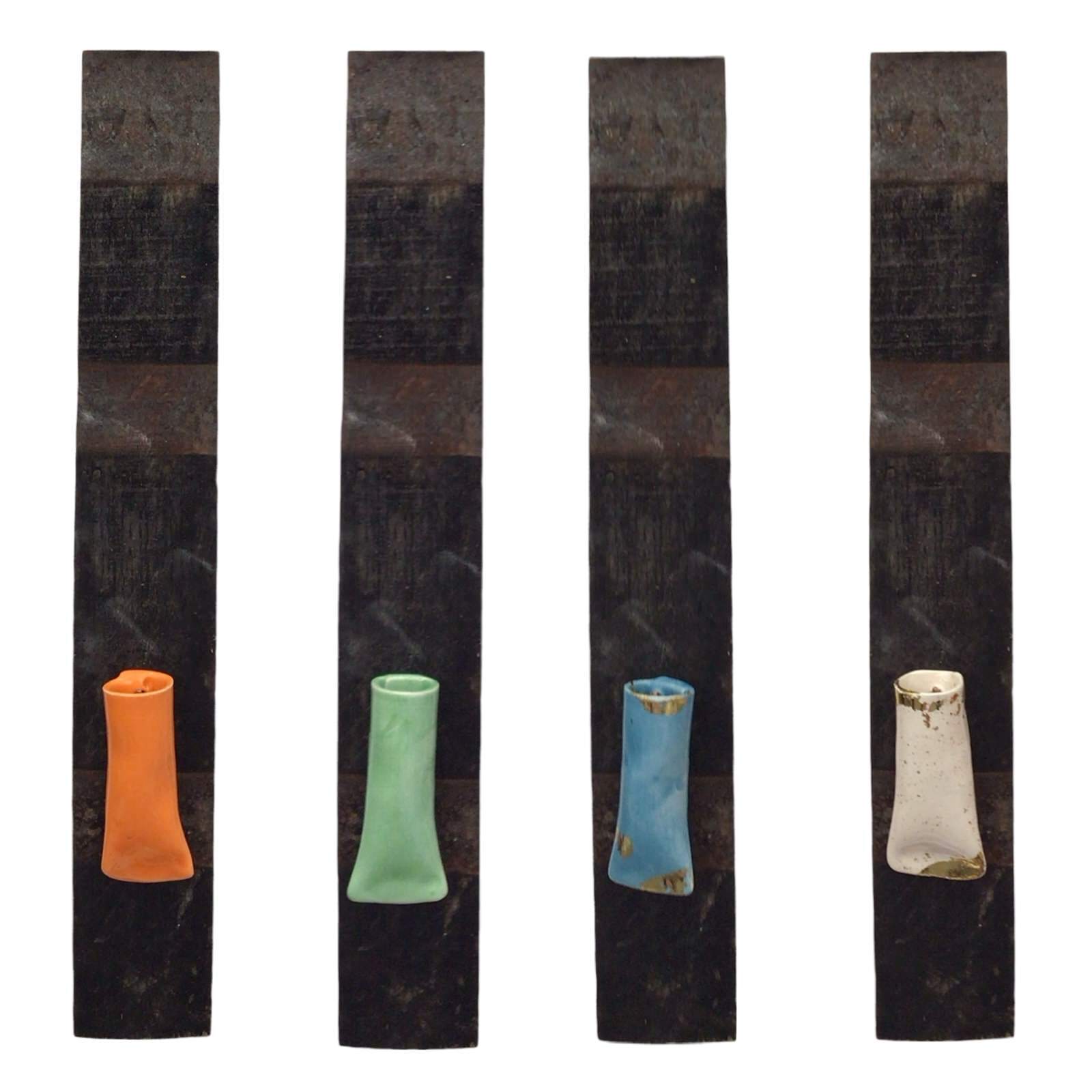 Four ceramic pocket vases in a vertical orientation, set against whisky barrel staves, with colors orange, green, and blue.