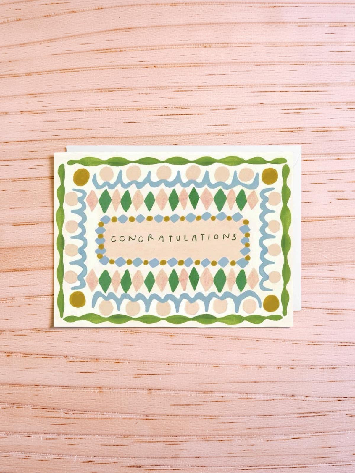 Greeting card with decorative border and 'Congratulations' text on a wooden surface.
