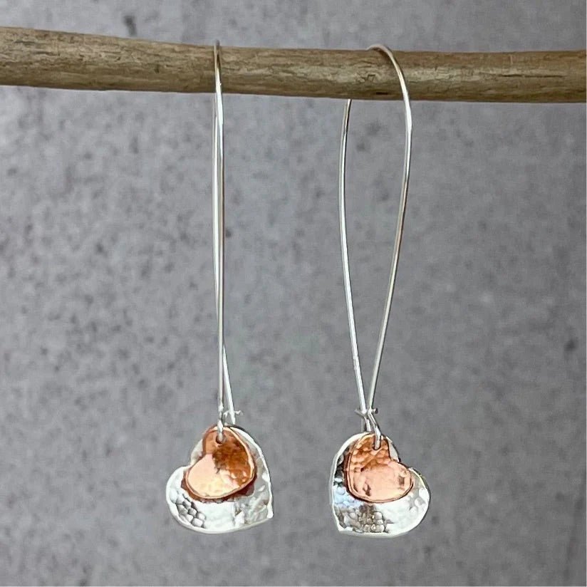 Pair of silver heart-shaped earrings with smaller copper on a gray background.