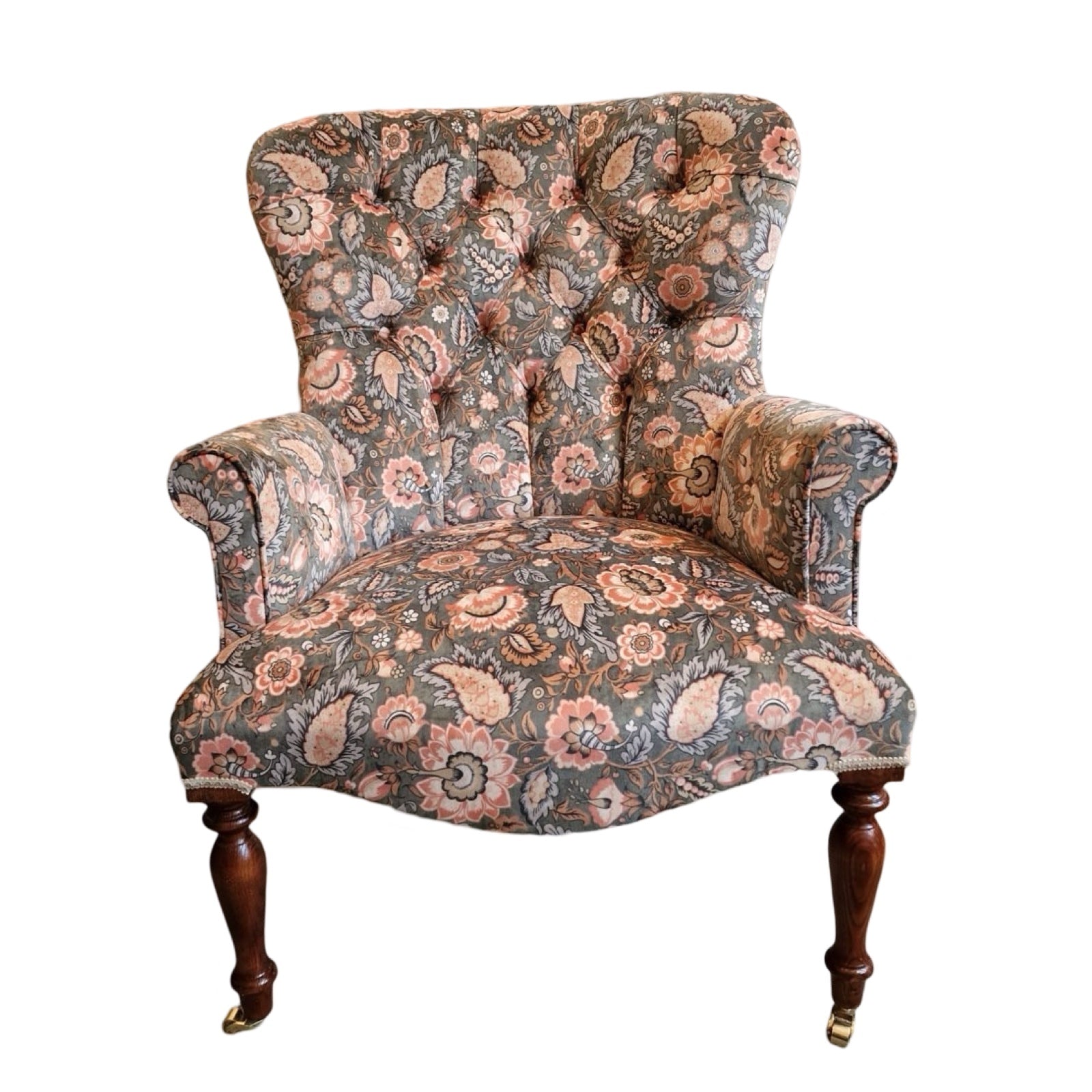 A luxurious armchair upholstered in light green/grey velvet with a floral pattern of coral flowers and pale blue leaves, featuring a button-back design, cream binding, and mahogany legs with gold castors.