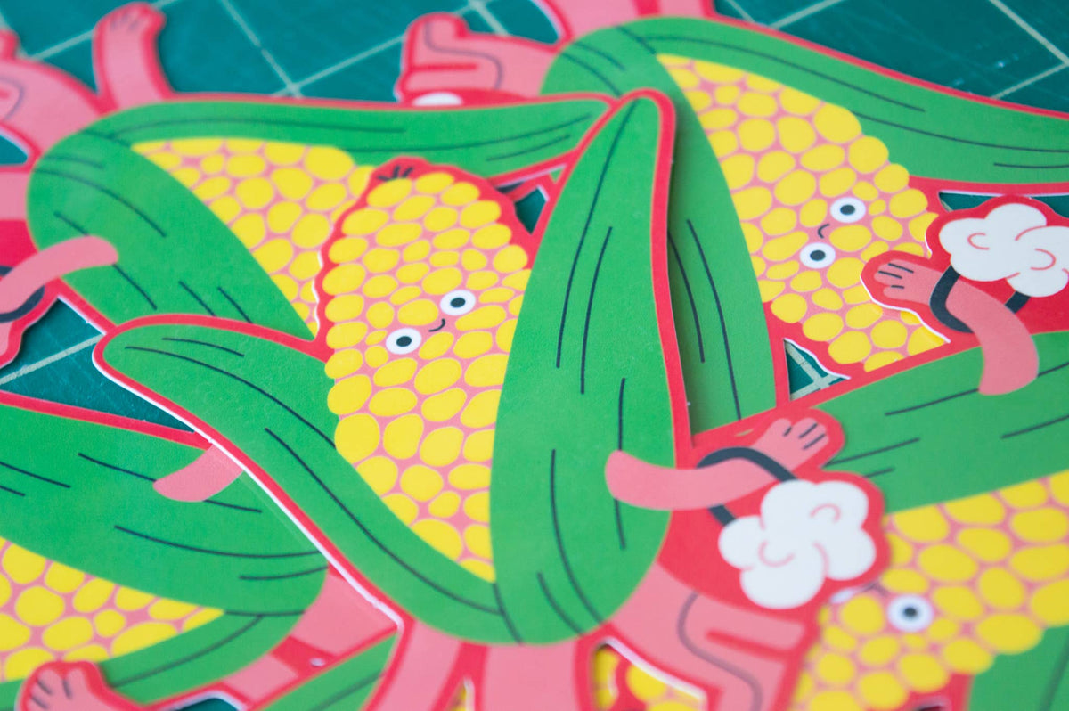 A close-up of colourful cartoon corn stickers layered over a green cutting mat background.