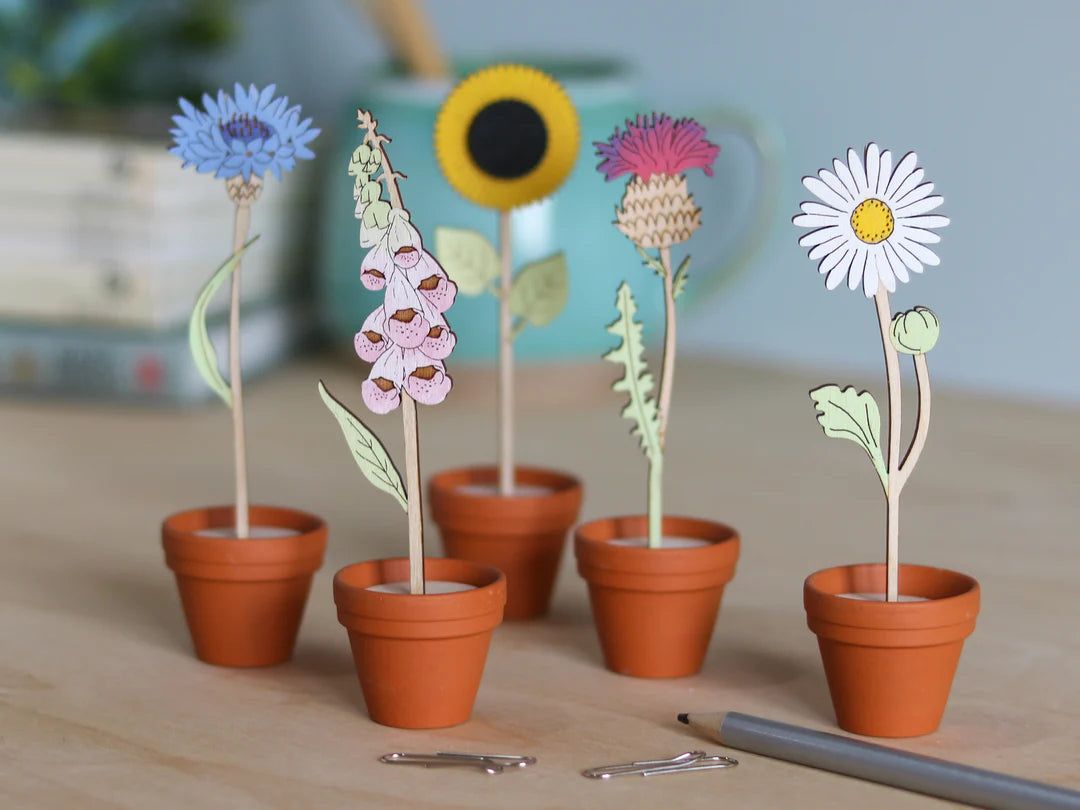 Set of wooden flowers in mini terracotta pots on a wooden surface.