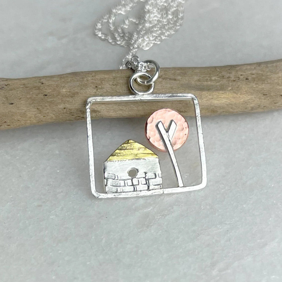 Necklace with a pendant featuring a small building and tree on a gray background.