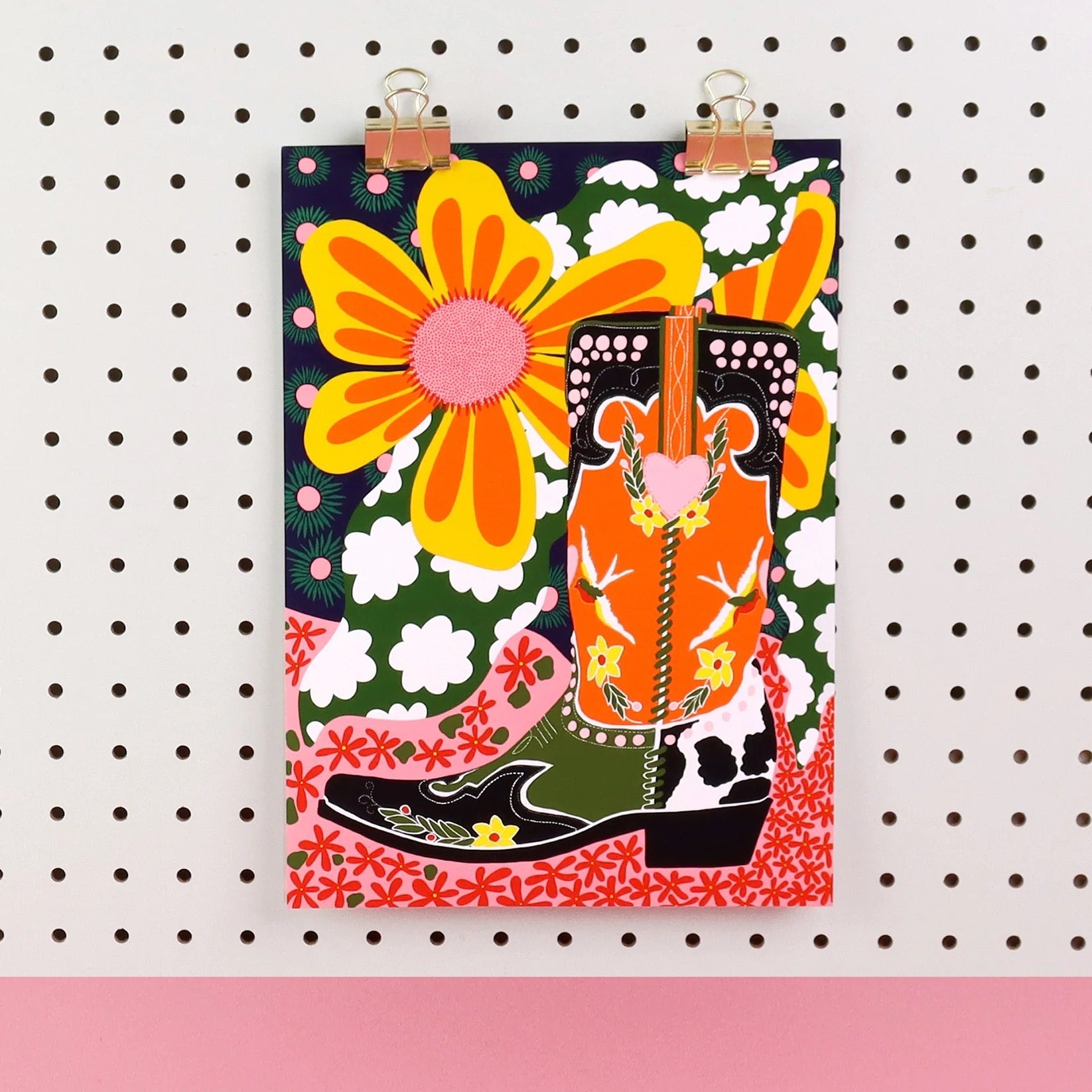 Colourful poster with cowboy boots and flowers on a pegboard background.