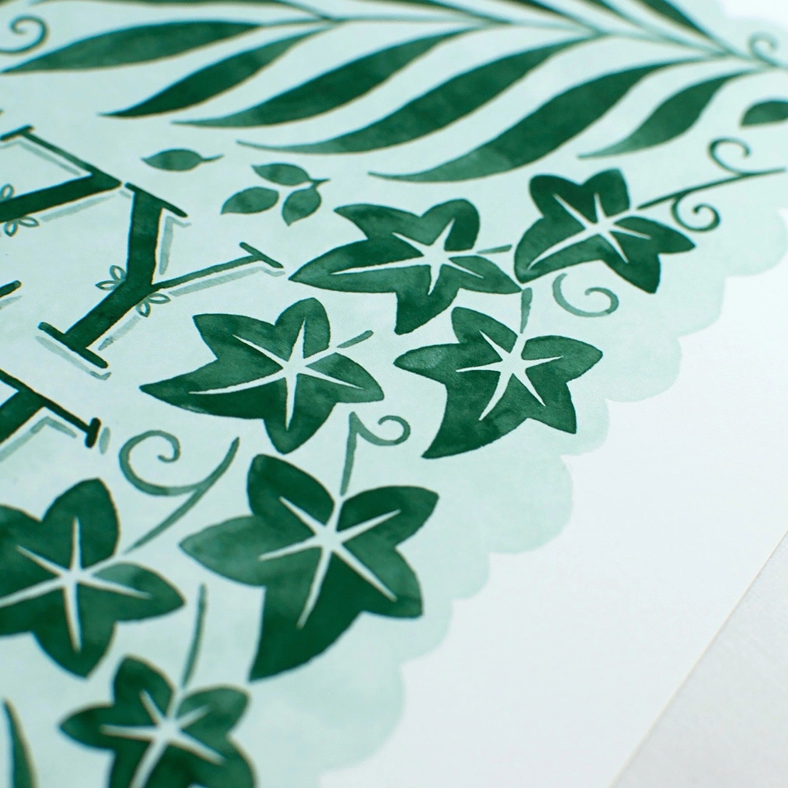 Decorative print with green leaf patterns and cut-out letters on a light blue background.